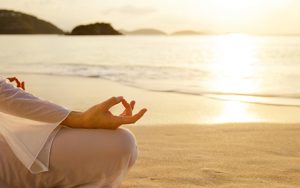 unrecognizable woman meditating at sunset on the beach in the Caribbean